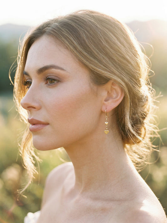 Woman with styled hair and golde heart earrings in a natural setting
