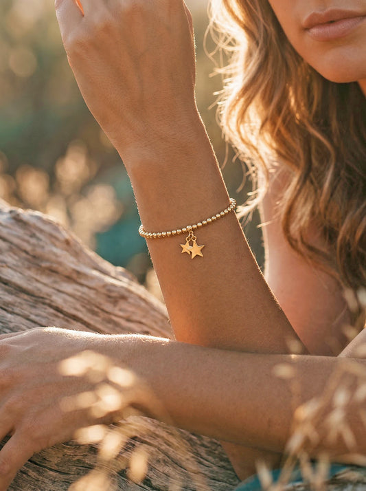 Close-up of a person's wrist wearing a gold bracelet with a star charm, sitting outdoors.