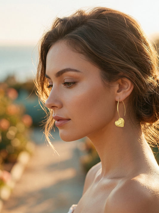 Woman wearing gold heart-shaped earrings with a blurred outdoor background