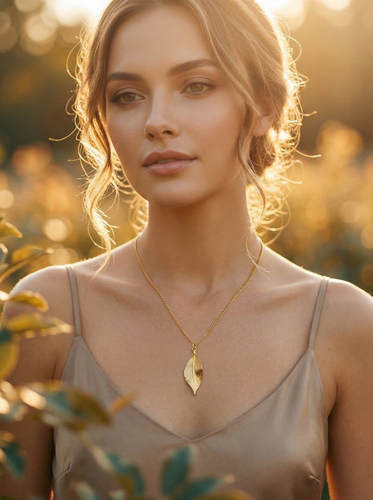 Woman wearing a gold necklace with a leaf pendant in a natural setting at golden hour