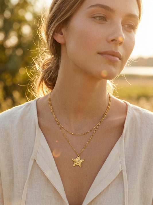 Woman wearing a gold-plated necklace with a star pendant in a natural golden hour setting