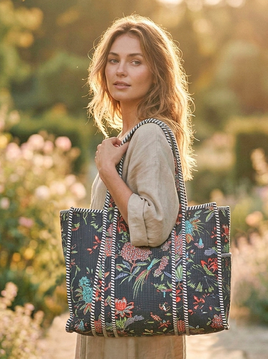 Woman holding a large black floral-patterned tote bag in a garden setting