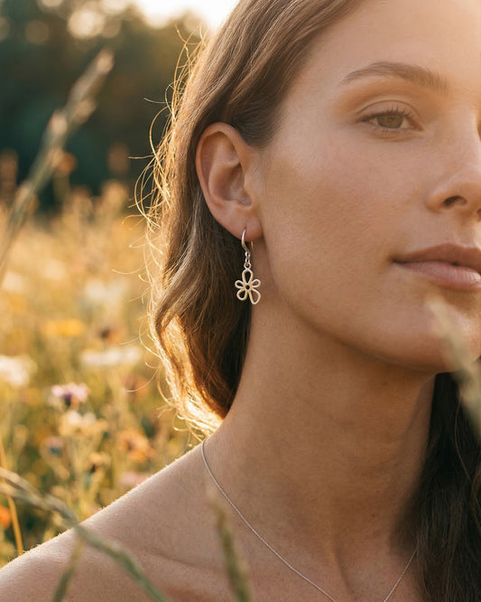 Woman wearing a silver flower earring in a natural setting with blurred background