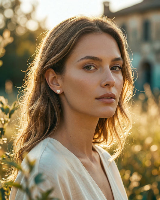 Woman with wavy hair standing outdoors with a blurred background wearing silver heart shaped earrings