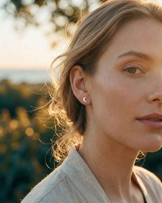 Close-up of a woman wearing a silver moon shaped earring with a blurred natural background