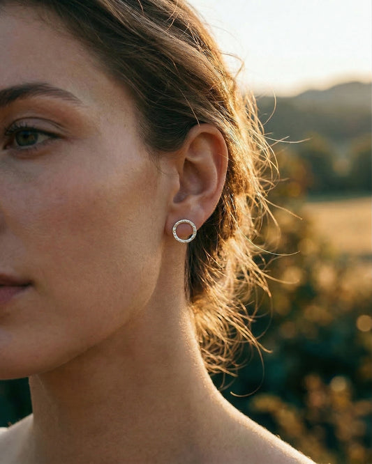 Close-up of a person wearing silver hoop earrings with a blurred natural background