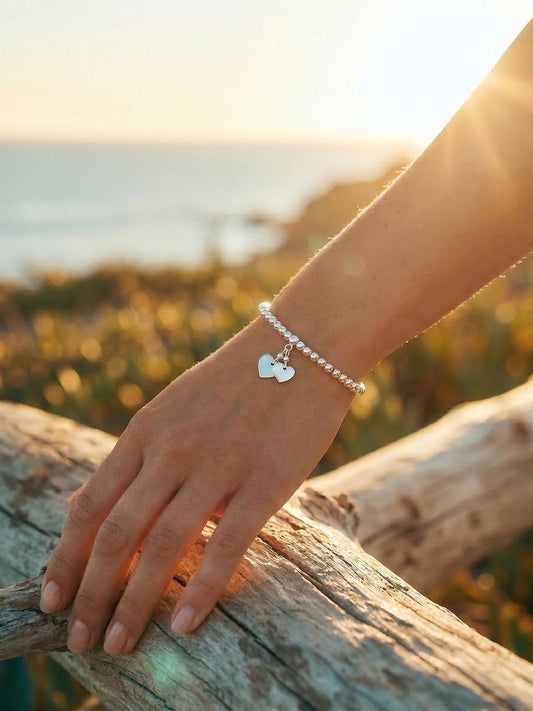 Hand wearing a bracelet with heart charms on a wooden log against a blurred natural background