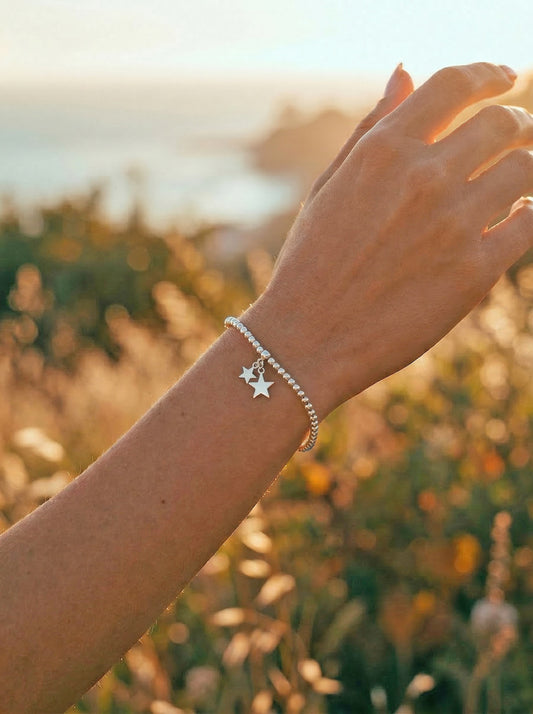 Hand wearing a silver bracelet with a star charm against a blurred natural background