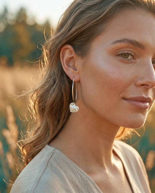 Woman wearing silver heart earrings with a blurred natural background