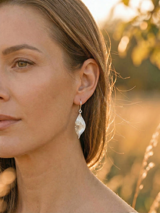Woman wearing silver leaf earrings with a blurred natural background