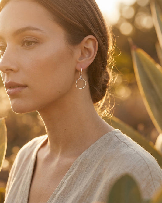 Woman wearing silver hoop earrings with a blurred natural background
