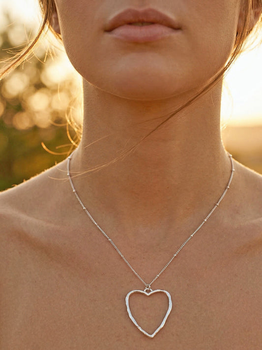Woman wearing a silver heart-shaped necklace with a blurred natural background