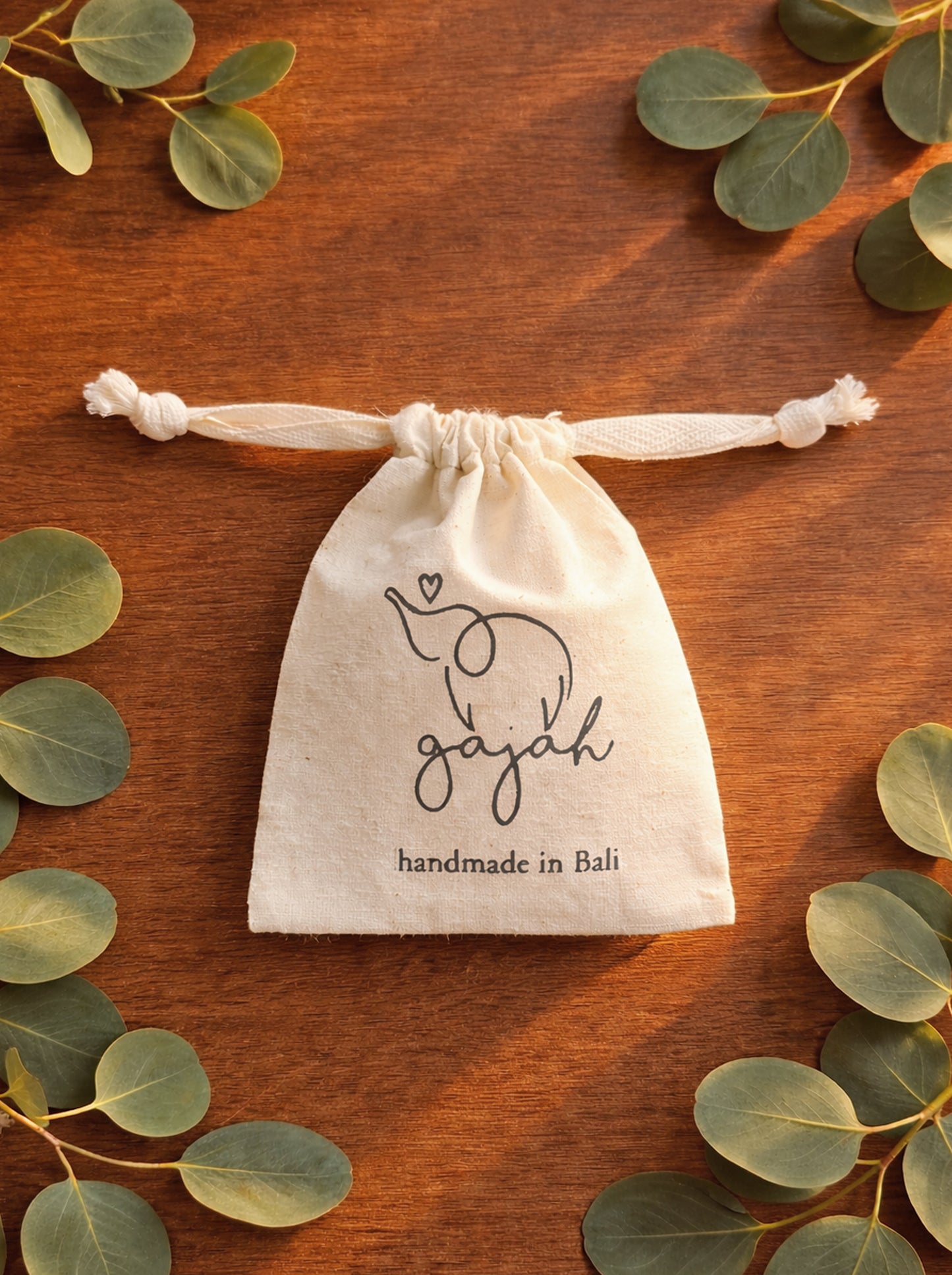 Drawstring unbleached cotton giftbag on wooden background with leaves