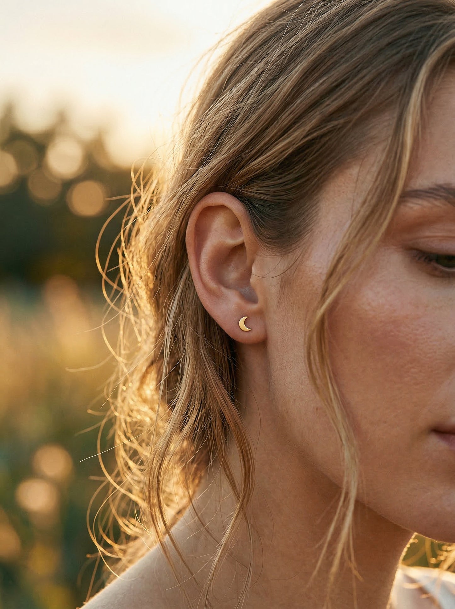 Close-up of a person wearing a gold moon shaped earring with a blurred natural background