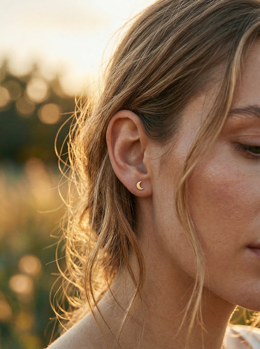Close-up of a person wearing a gold moon shaped earring with a blurred natural background