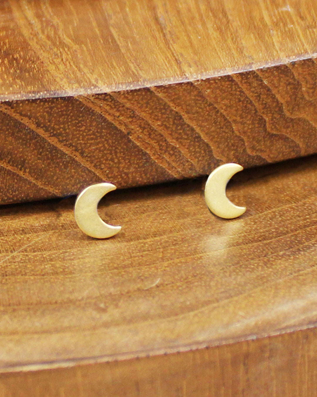 Gold crescent moon earrings on a wooden surface