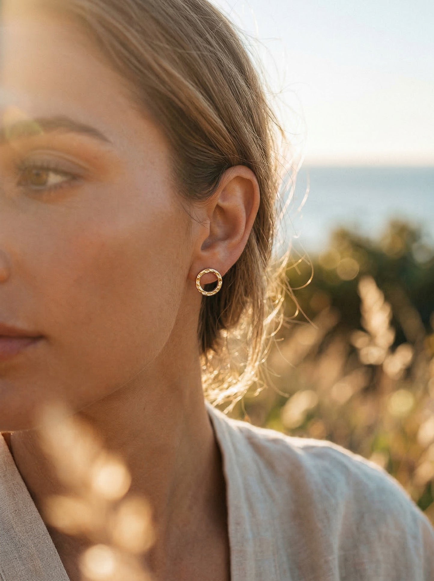 Close-up of a person wearing gold hoop earrings with a blurred natural background