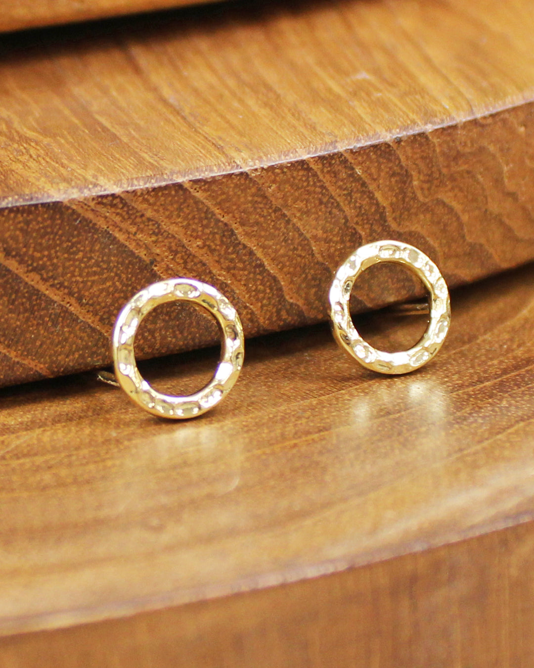Gold circle stud earrings on a wooden surface
