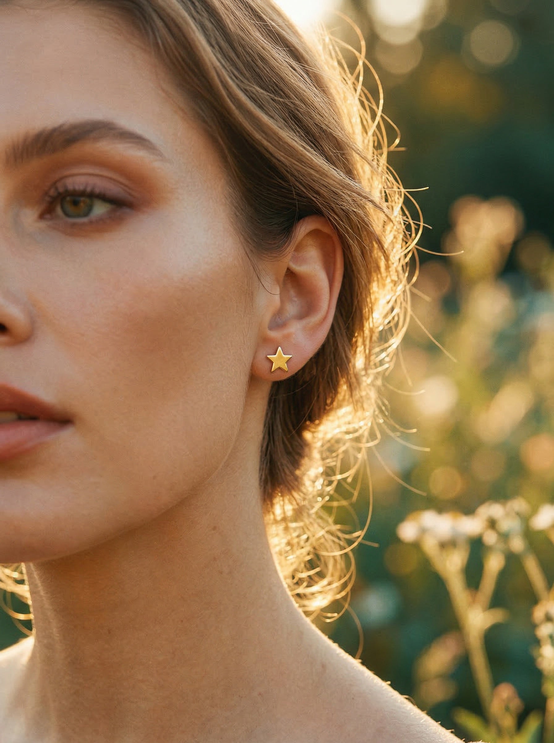 Close-up of a woman wearing gold star earrings with a blurred natural background