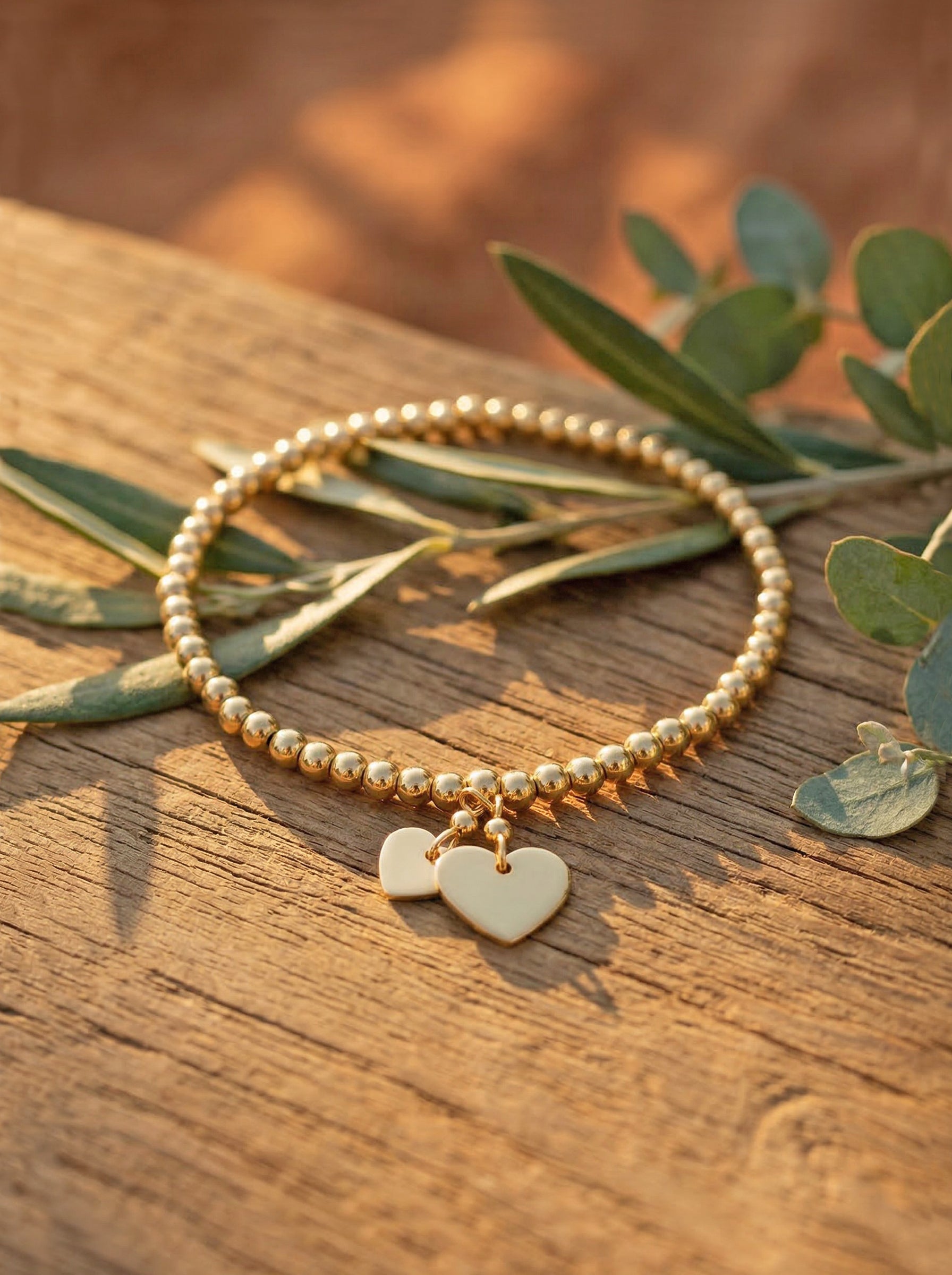 Gold bracelet with heart charm on a wooden surface with leaves