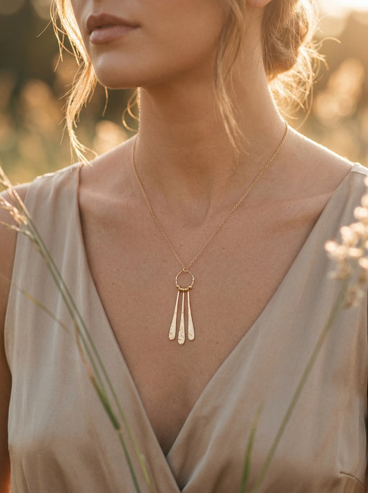 Woman wearing a gold necklace with a pendant in a natural setting at golden hour