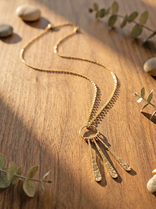 Gold necklace on a wooden surface with leaves and stones