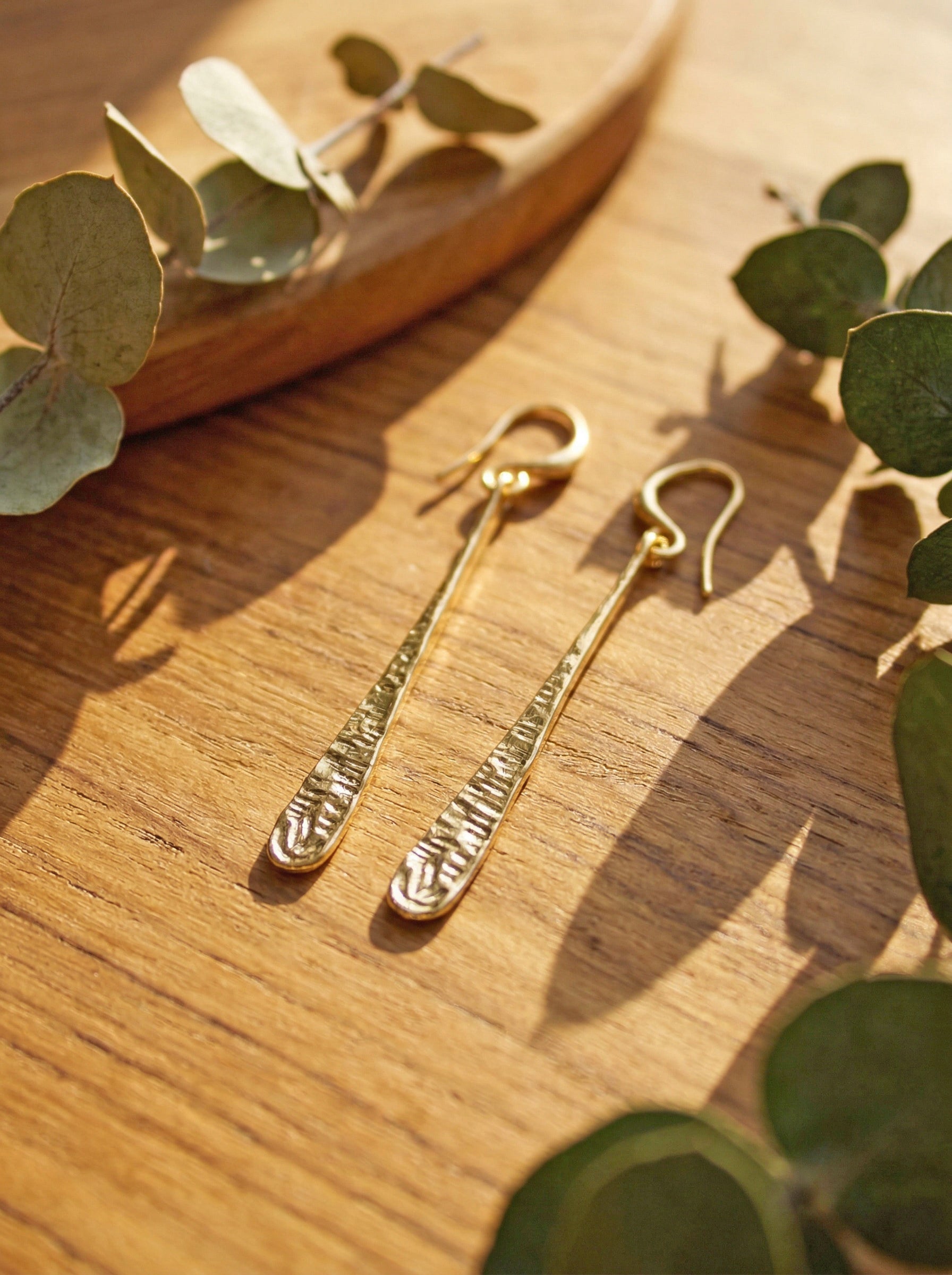 Gold earrings on a wooden surface with green leaves
