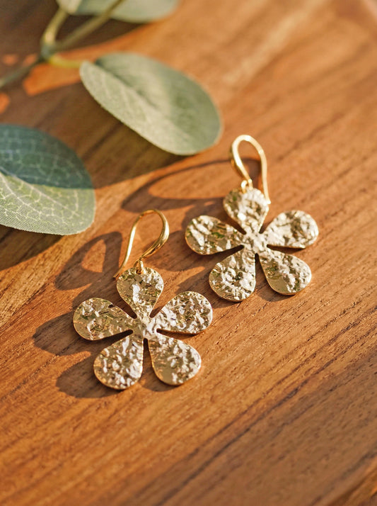Gold flower-shaped earrings on a wooden surface with green leaves.