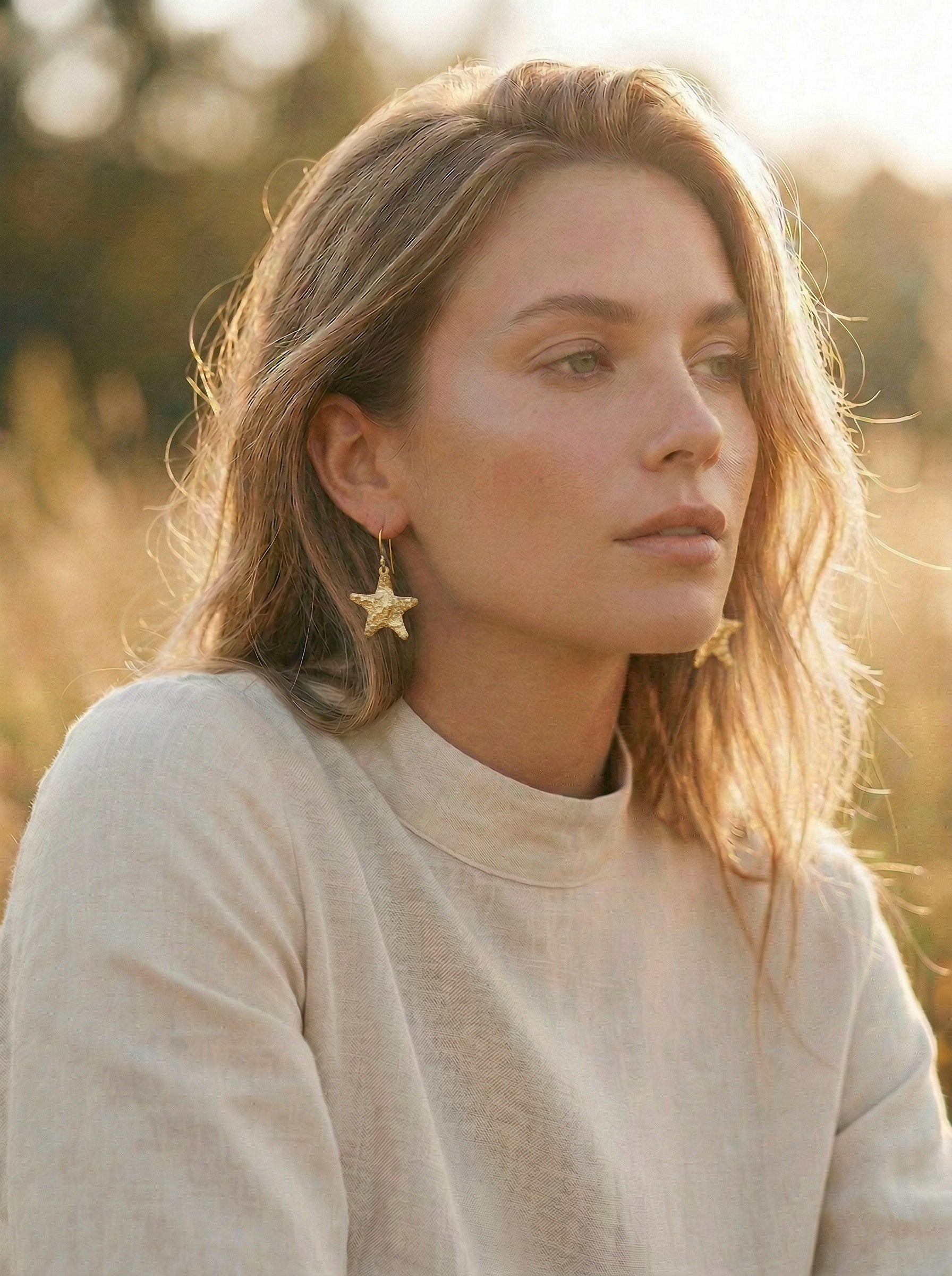 Woman wearing a gold star-shaped earring in a natural setting
