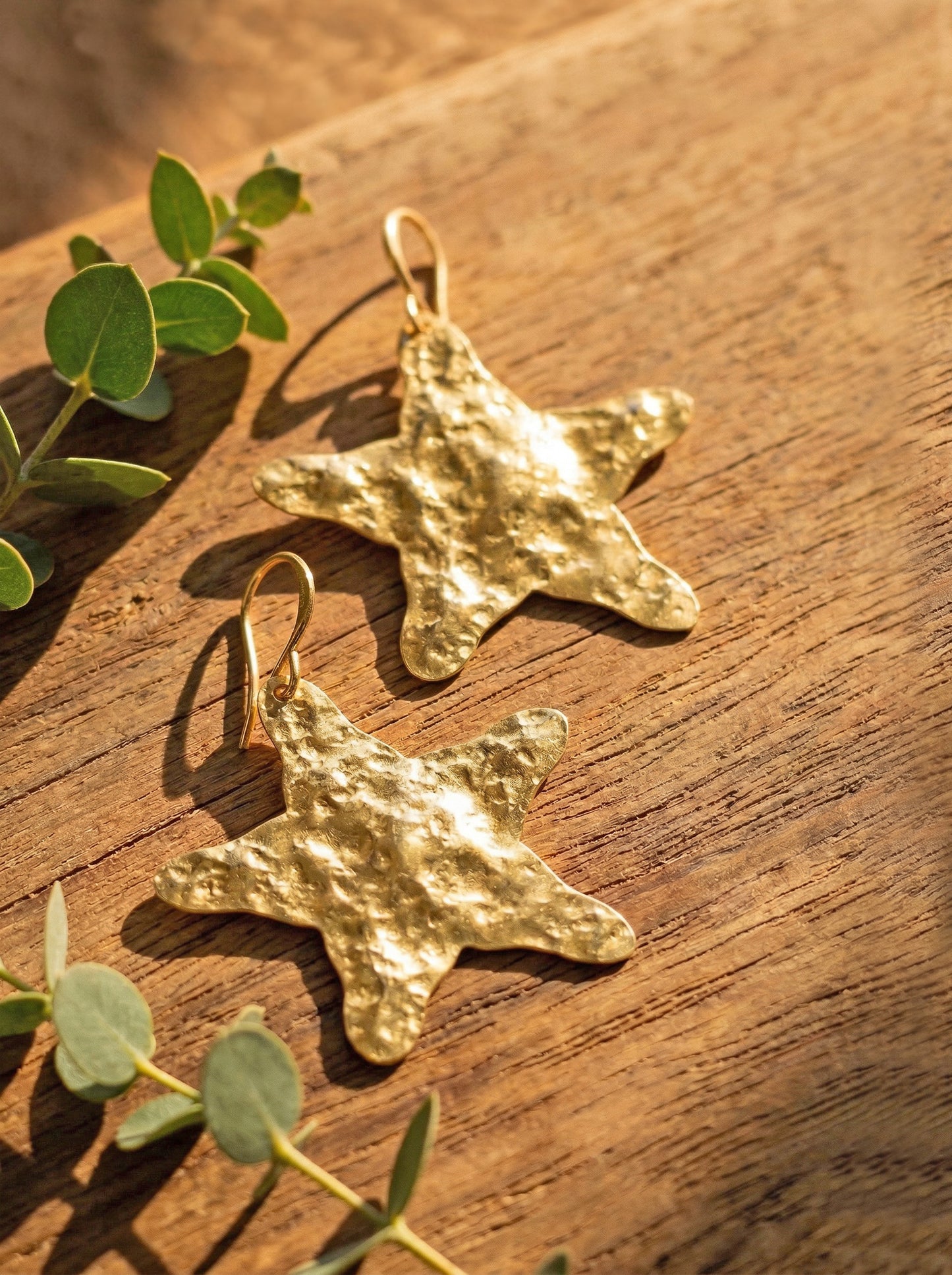 Gold star-shaped earrings on a wooden surface with green leaves.