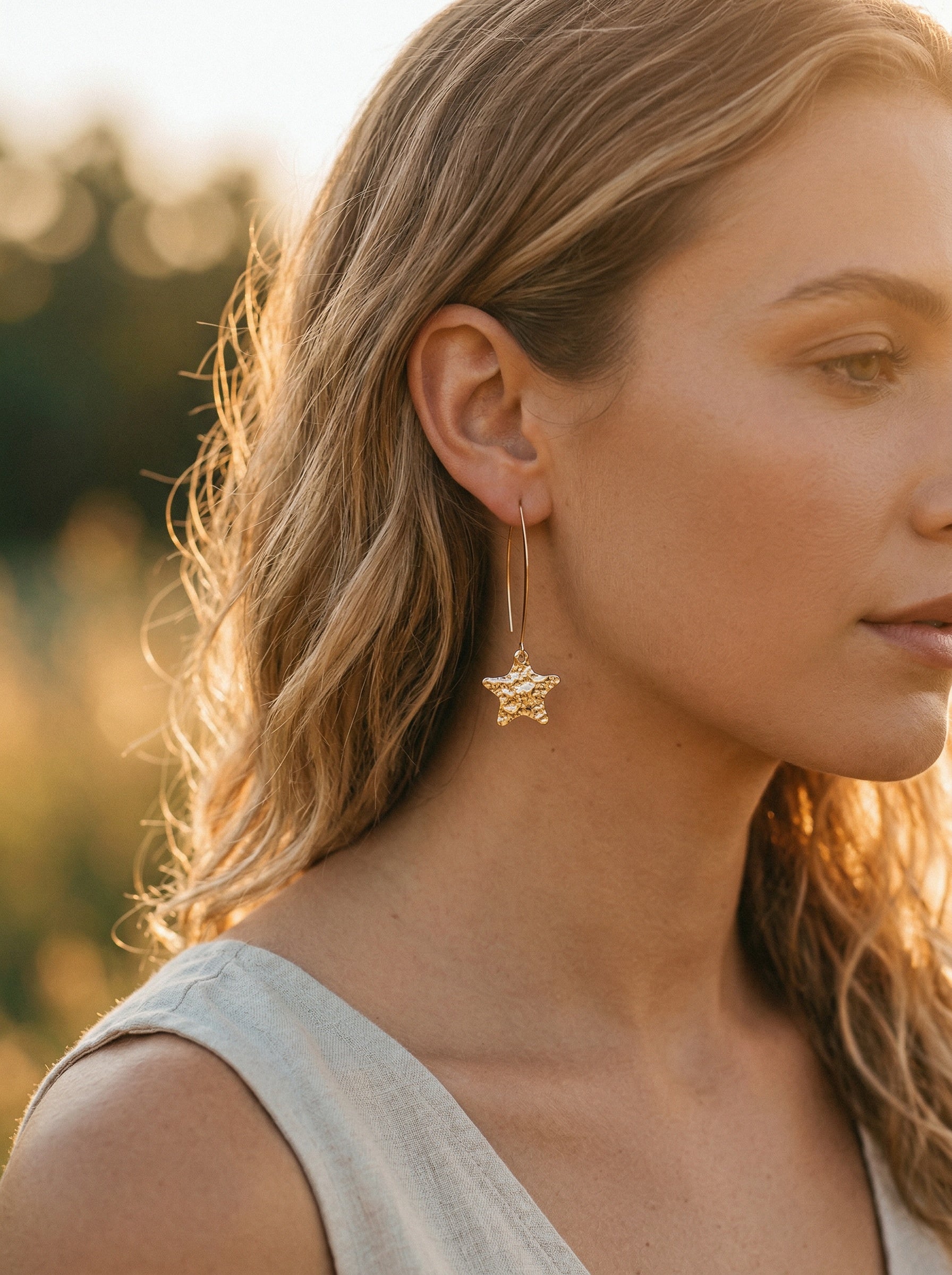 Close-up of a woman wearing gold star-shaped earrings with a blurred natural background