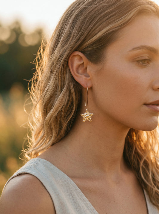 Close-up of a woman wearing gold star-shaped earrings with a blurred natural background
