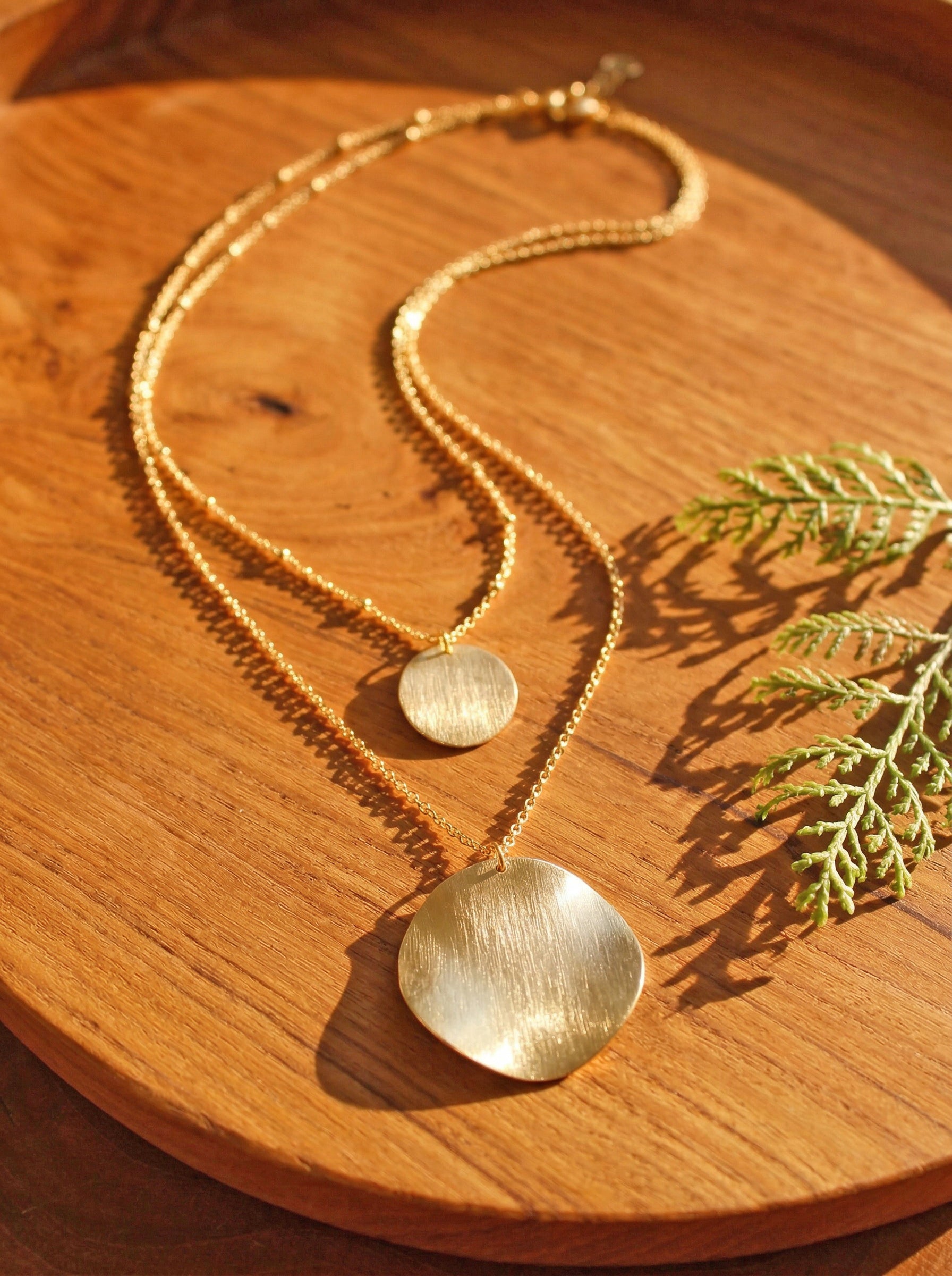Gold necklace with round pendants on a wooden surface with green leaves.