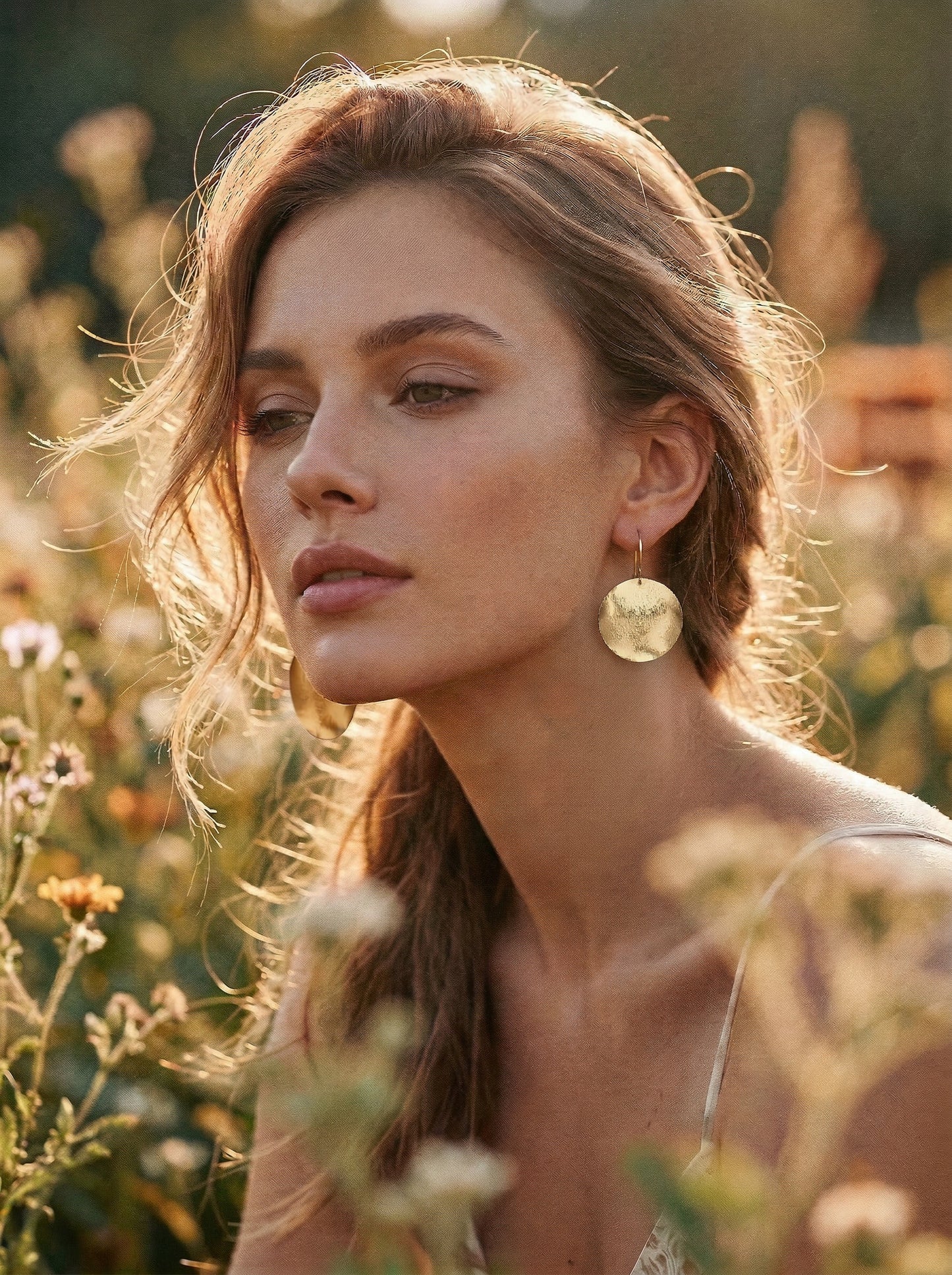 Woman with large gold disc earrings standing in a field of flowers