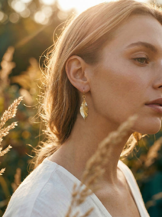 Woman wearing gold leaf earrings in a natural setting