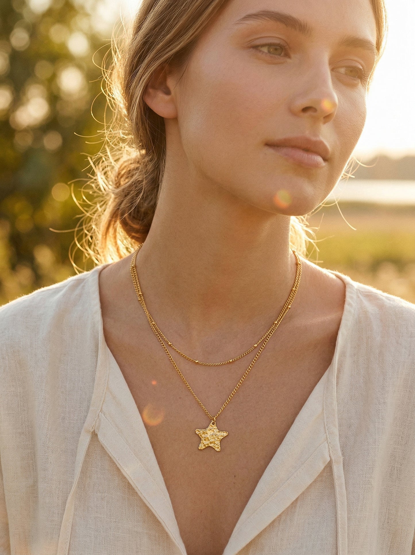 Woman wearing a gold-plated necklace with a star pendant in a natural golden hour setting