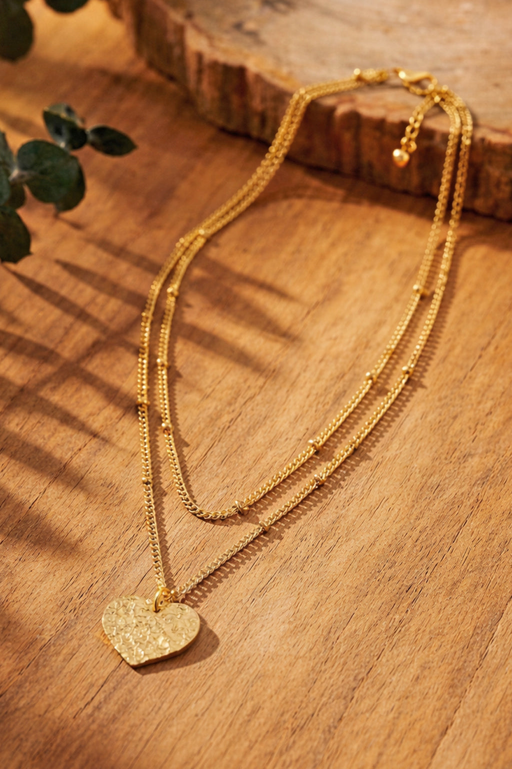 Gold-plated necklace with a hammered heart pendant on a wooden surface