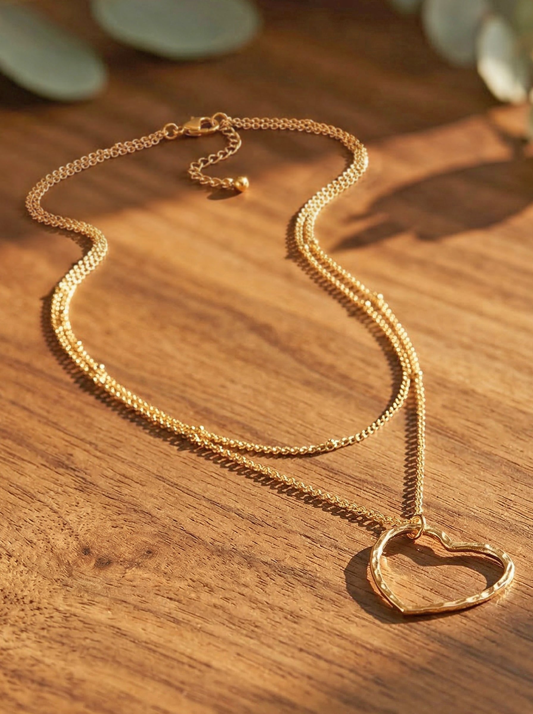 Gold layered necklace with a heart pendant on a wooden surface
