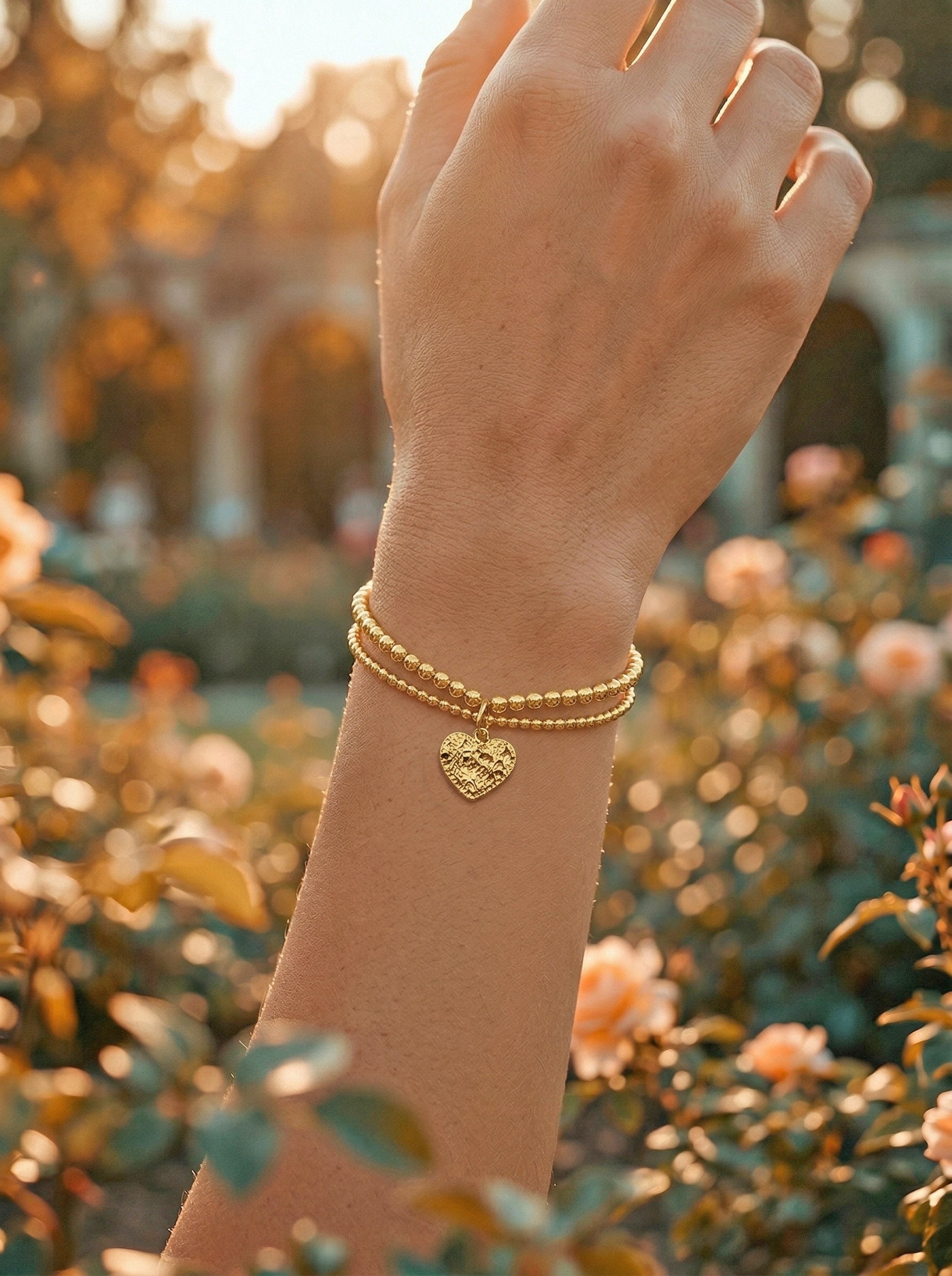 Gold bracelet with a heart charm on a wrist against a blurred garden background