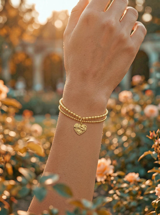 Gold bracelet with a heart charm on a wrist against a blurred garden background
