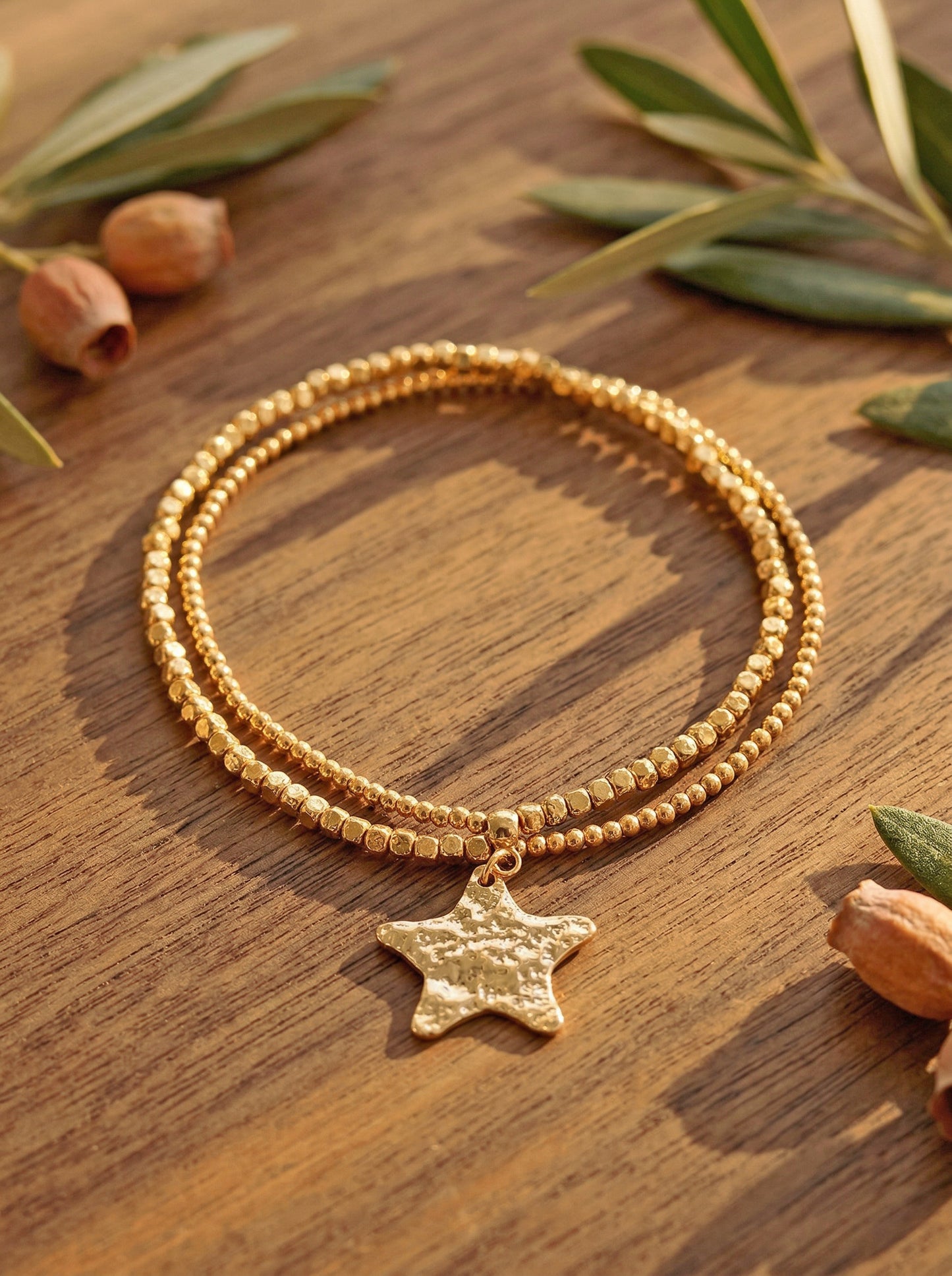 Gold bracelet with a star charm on a wooden surface with leaves and nuts.