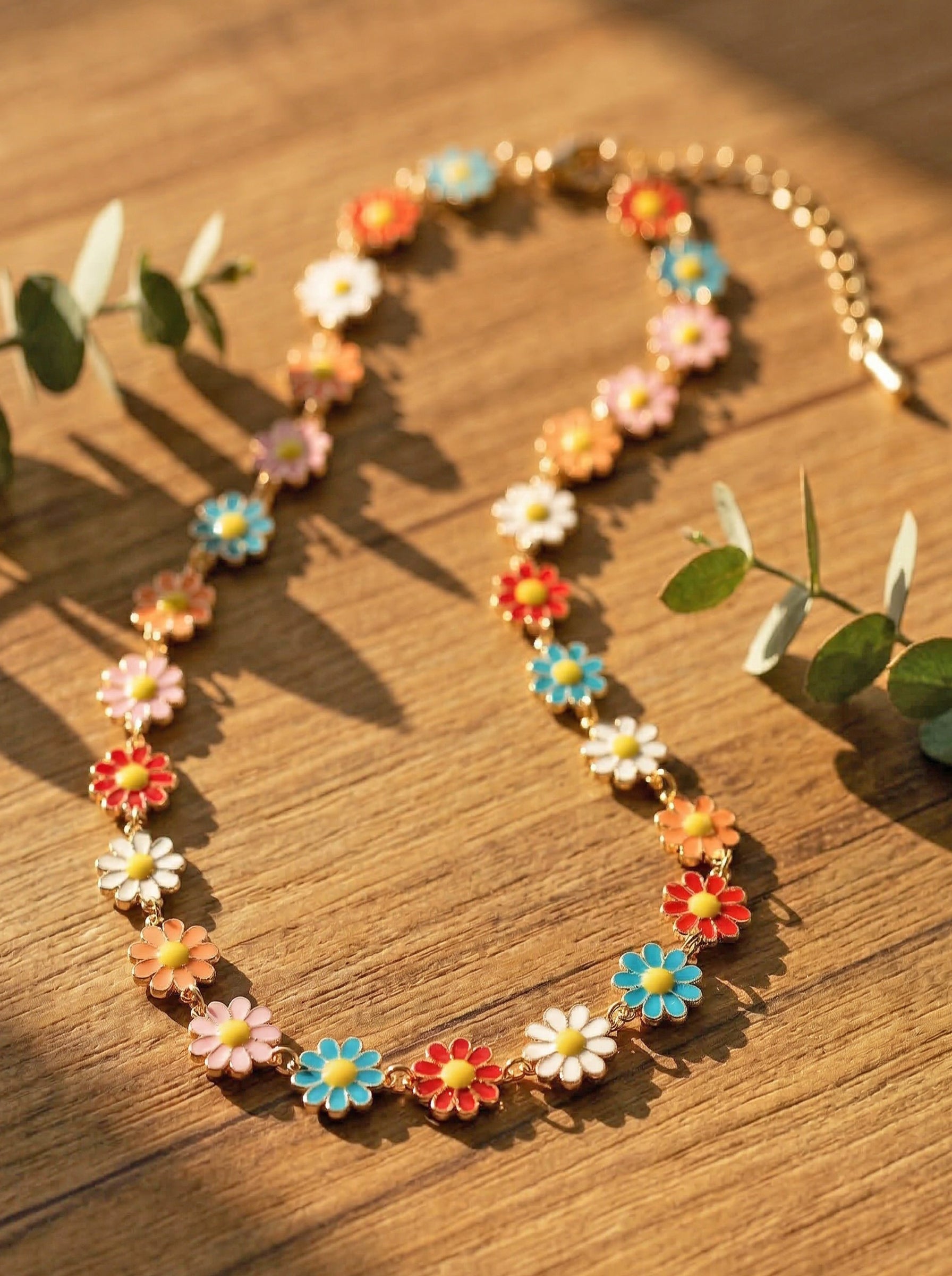 multicoloured daisy necklace on a wooden surface with green leaves.