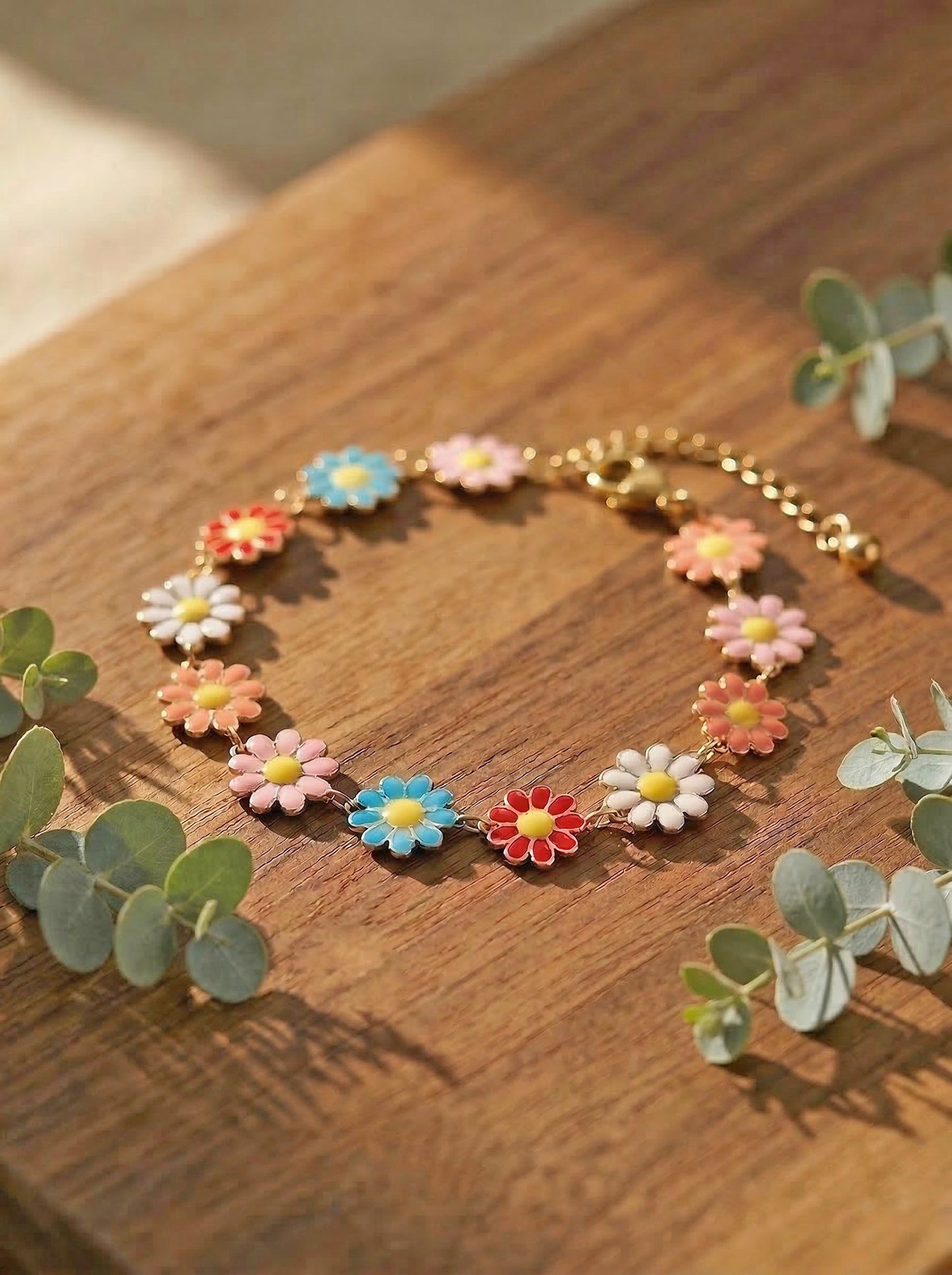 Multicoloured daisy bracelet on a wooden surface with eucalyptus leaves.