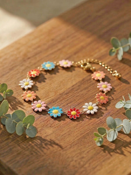 Multicoloured daisy bracelet on a wooden surface with eucalyptus leaves.