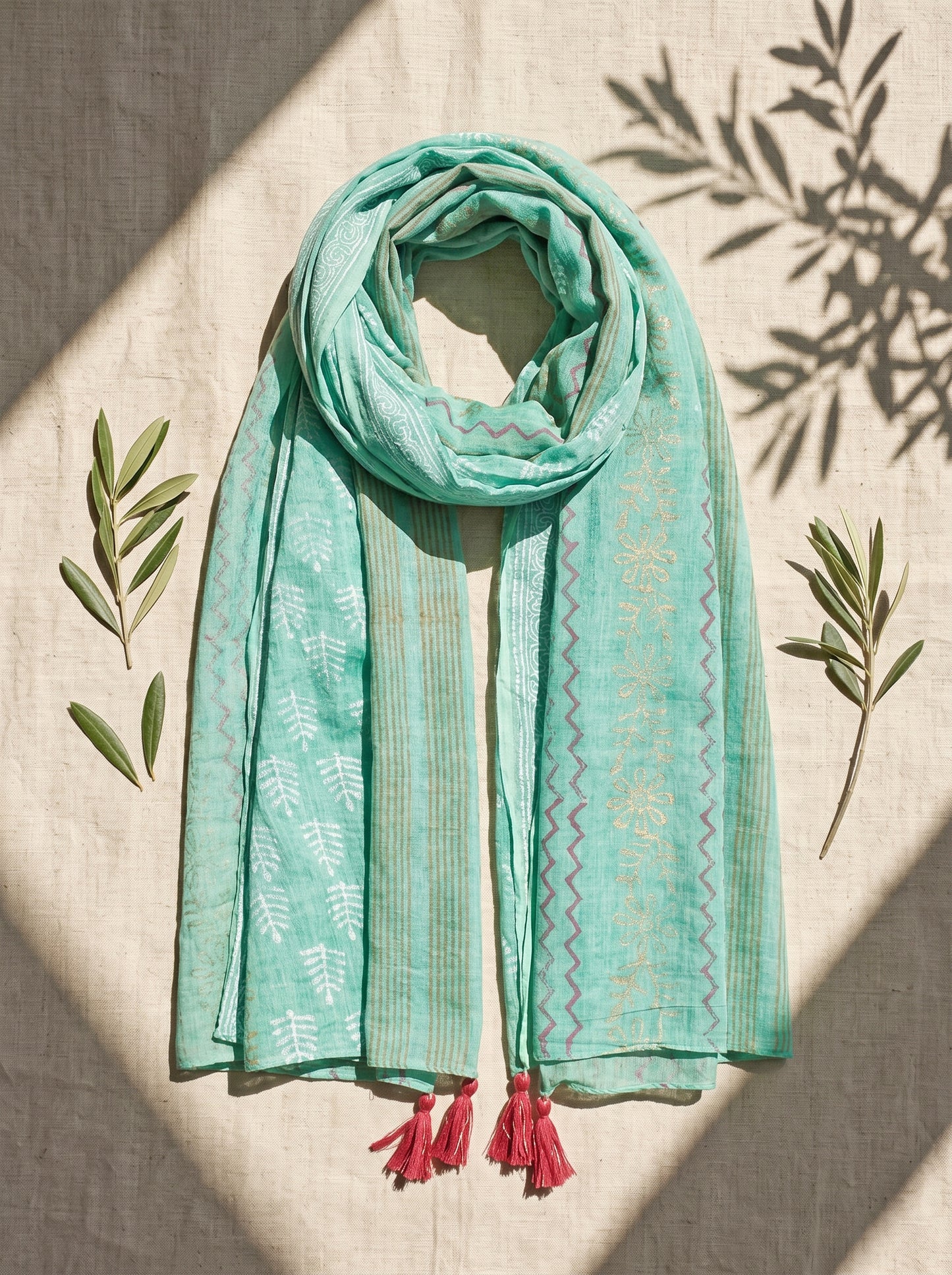 Turquoise black printed scarf with  on a beige surface with green leaves.
