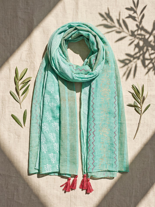 Turquoise black printed scarf with  on a beige surface with green leaves.
