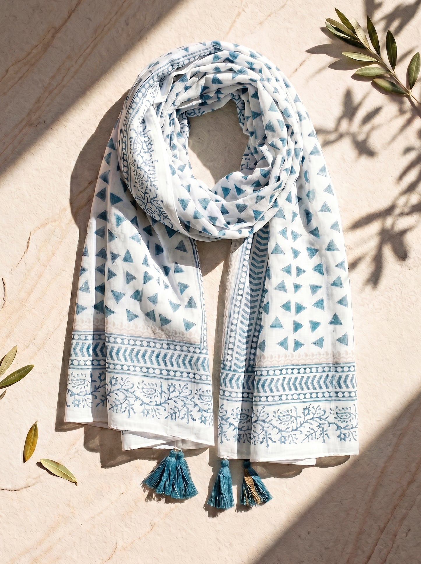 White scarf with blue geometric patterns and tassels on a wooden surface with leaves.