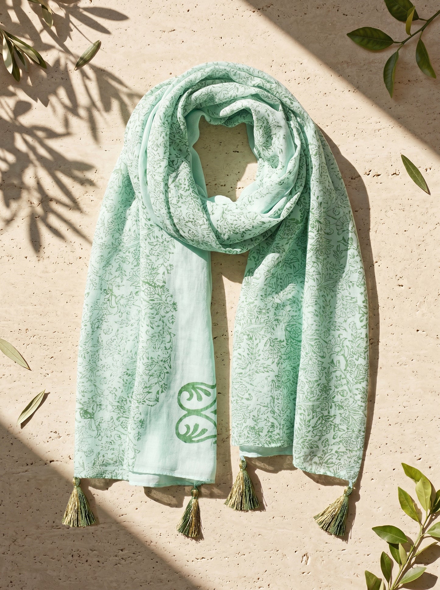 Mint green scarf with tassels on a beige surface with leaf decorations.