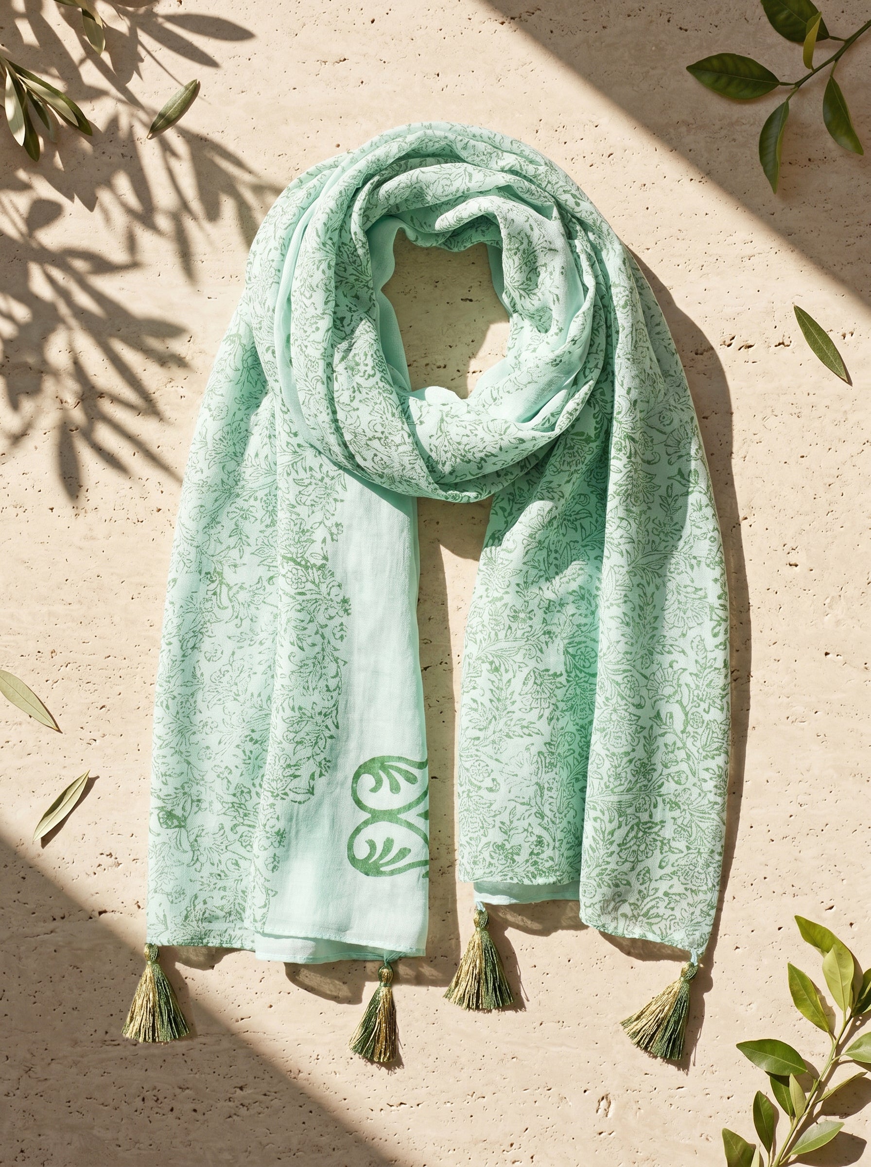 Mint green scarf with tassels on a beige surface with leaf decorations.