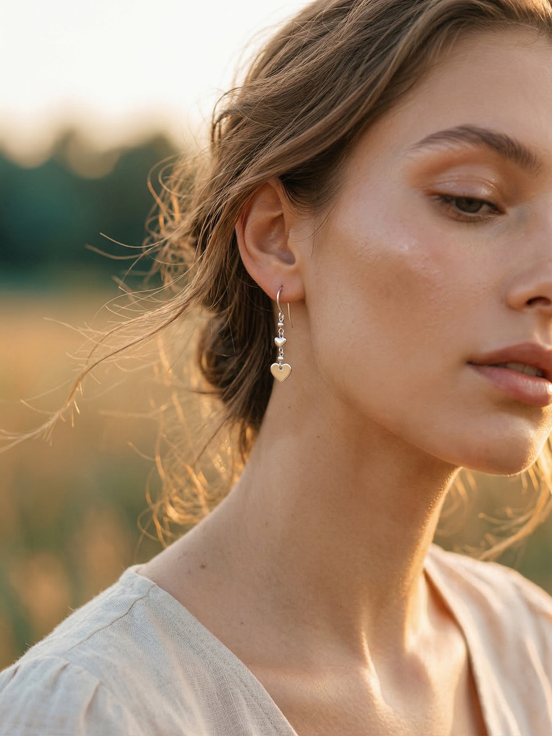 Close-up of a woman wearing silver heart earrings with a blurred natural background